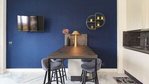 A modern kitchen with a dark blue accent wall, a flat-screen TV, a gold-framed shelf with plants, and a marble floor. - Dolce Vita Baveno (Baveno)