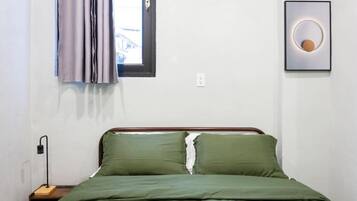 A bedroom with a bed, a nightstand, a wall-mounted light, a window with curtains, and a framed picture.