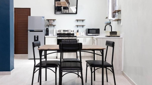 A compact kitchen with a dining table and four chairs, a refrigerator, a microwave, and a stove.