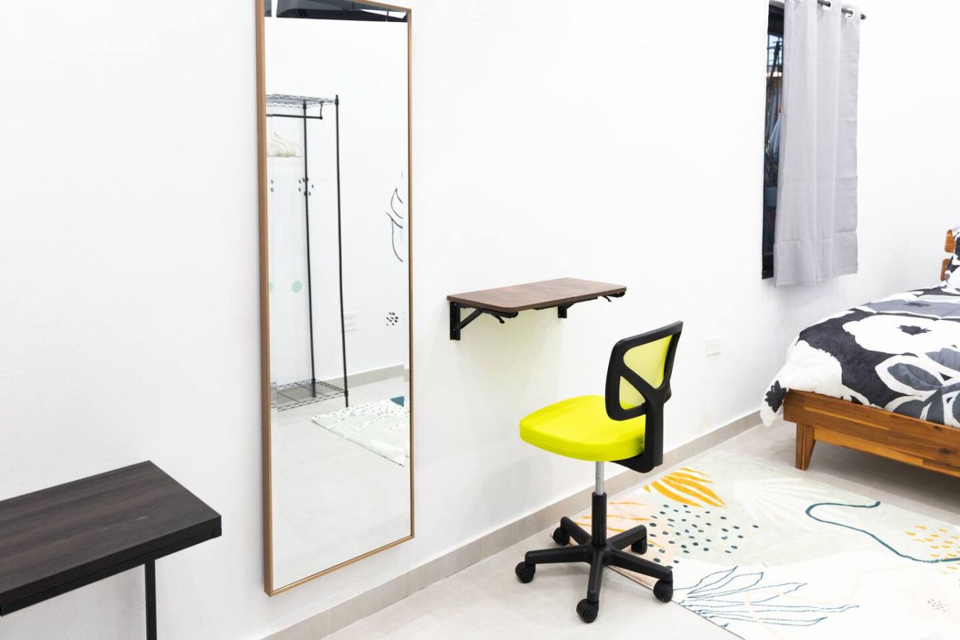 Een slaapkamer met een bed, een stoel, een bureau, een spiegel en een plank.