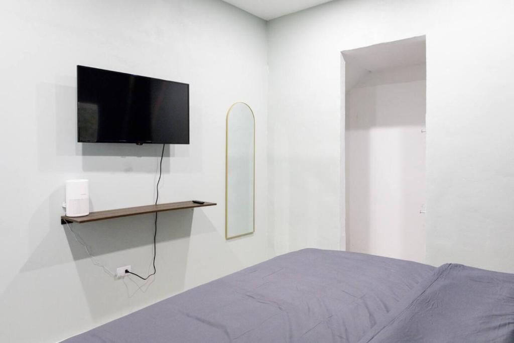 A minimalist room with a bed, a mounted TV, and a small shelf with a mirror.