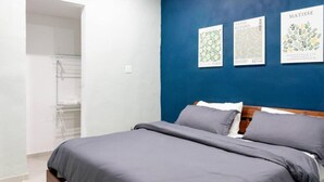 A bedroom with a bed, a blue accent wall, and three framed botanical prints.