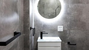 A modern bathroom with a round mirror, a white sink, and a black faucet.