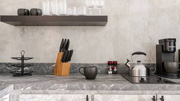 A kitchen with a marble countertop, a coffee maker, a kettle, a knife block, a spice rack, and a shelf with glasses and cups.