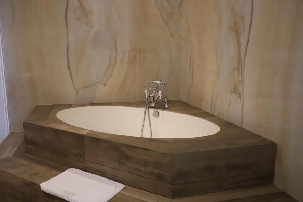 Un baño moderno con una bañera independiente, escalones de madera y una pared de mármol.
