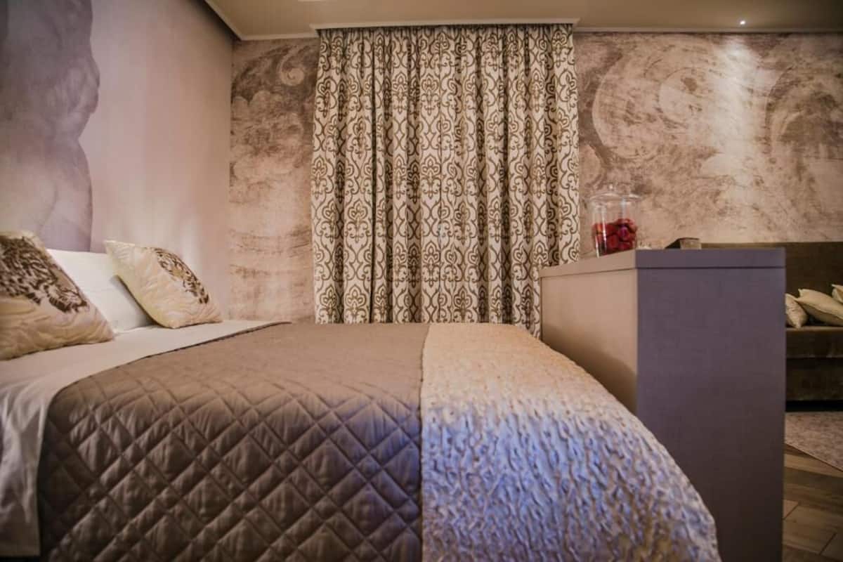 A bedroom with a bed, patterned curtains, and a marble wall.