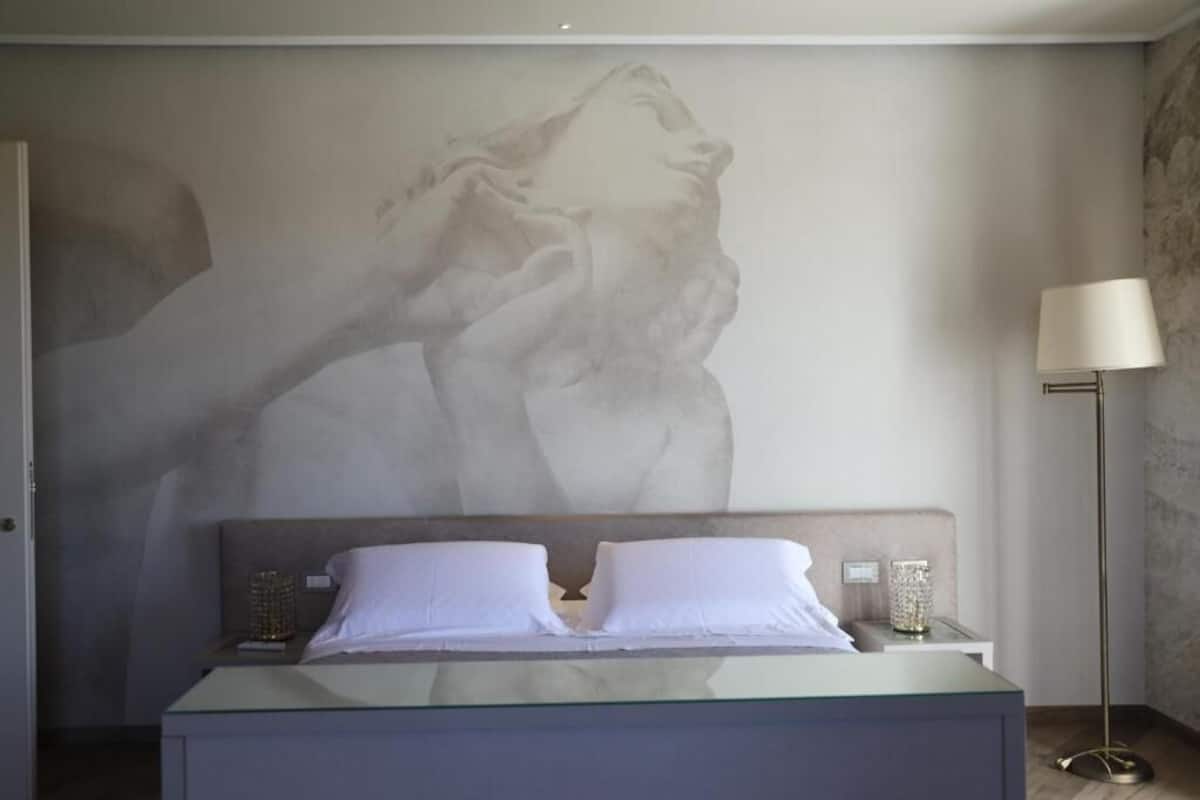 A bedroom with a bed, a nightstand, a lamp, and a large wall mural.