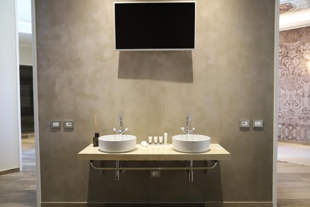 A modern bathroom with two sinks, a mounted TV, and a towel rack.