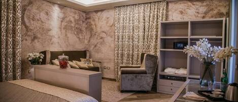 A bedroom with a bed, a seating area, a vanity with a mirror, and a shelving unit.