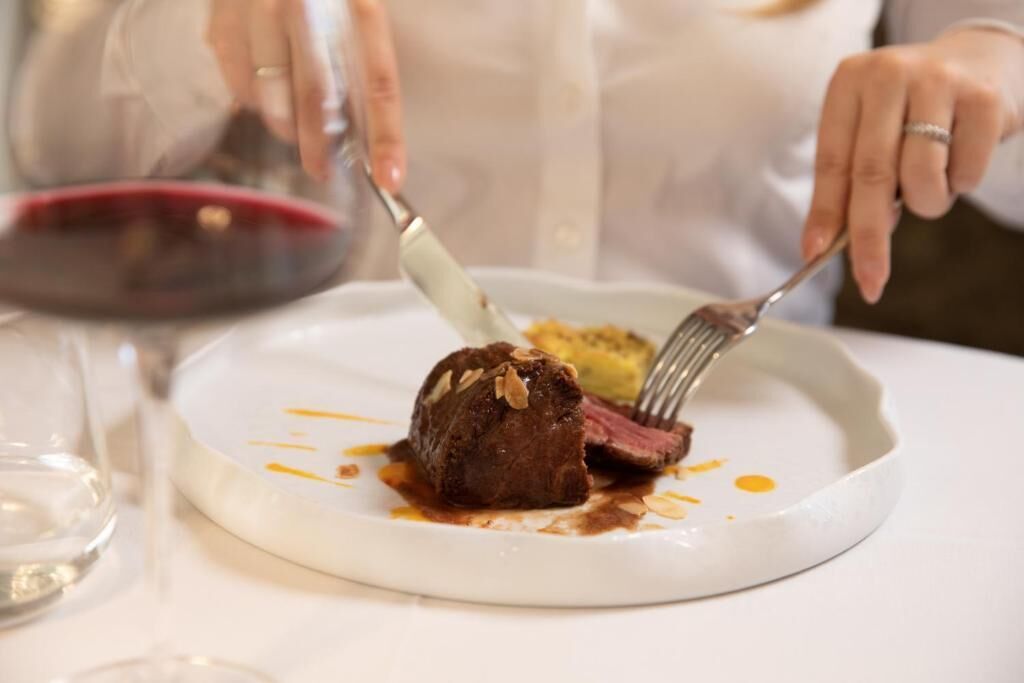 Una persona cortando un filete en un plato blanco con tenedor y cuchillo.