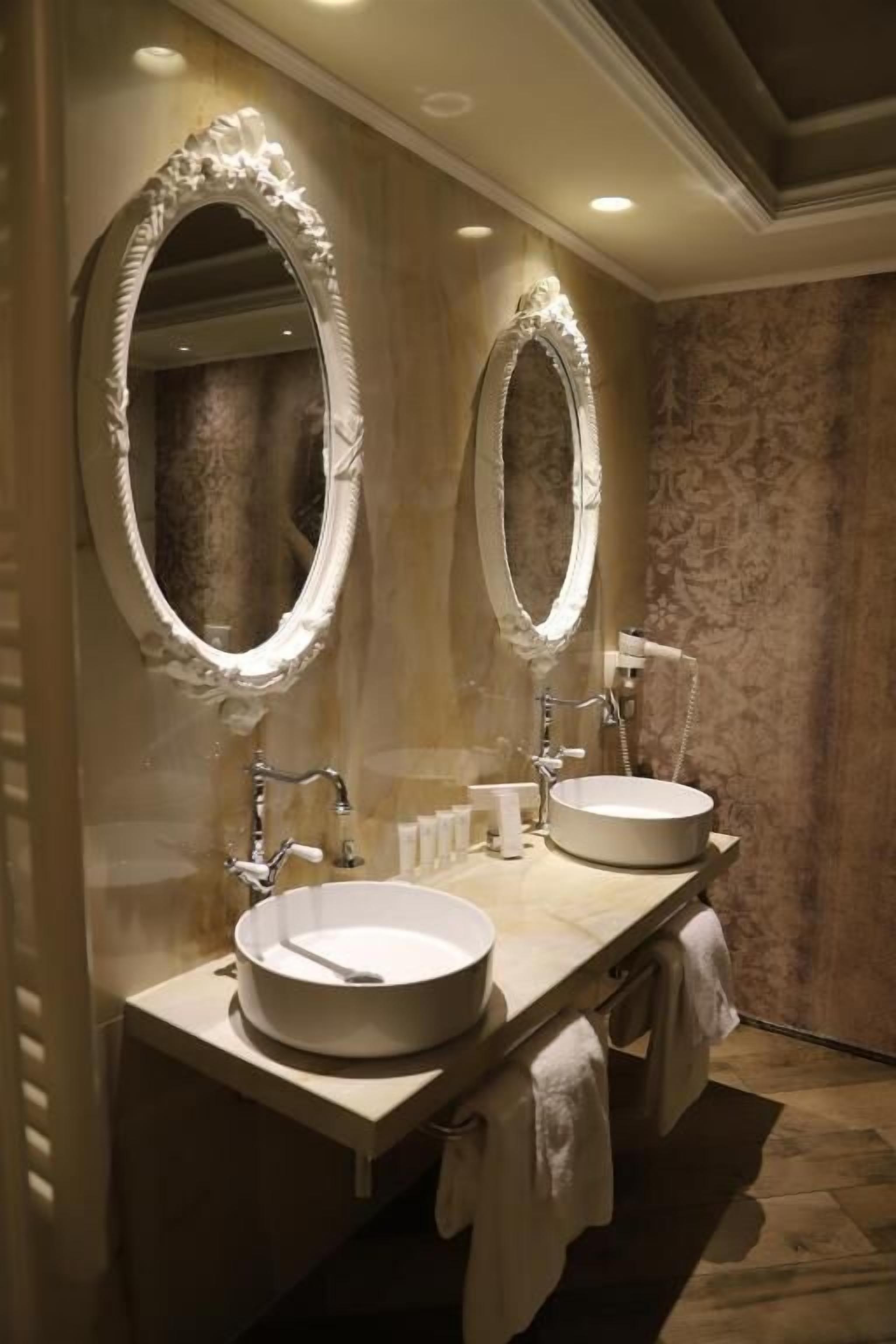 A bathroom with two large oval mirrors, a round sink, and a handheld showerhead.