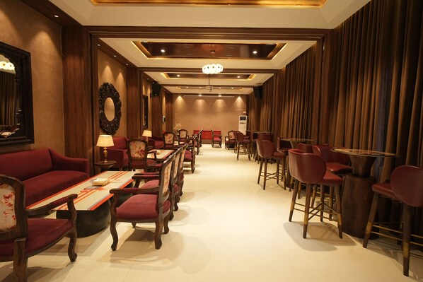 A hotel lobby with a long reception desk, red upholstered chairs, and a chandelier.