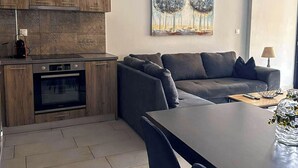 Eine moderne Küche mit Holzschränken, einem eingebauten Backofen und einem Essbereich mit einem dunkelgrauen Tisch und Stühlen.