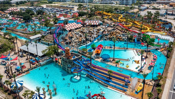 An aerial view of a water park with multiple pools, slides, and a large central pool area.