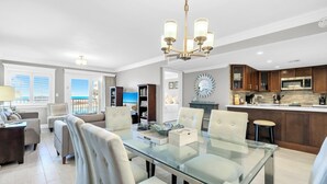 A modern kitchen with a glass dining table, white chairs, and a chandelier.