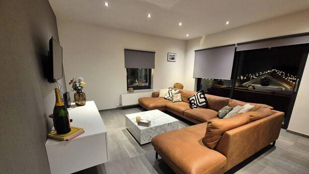 A modern living room with a sectional sofa, a white coffee table, and a flat-screen TV mounted on the wall. - Modern Apartment in a Prime Location! (Tongeren)