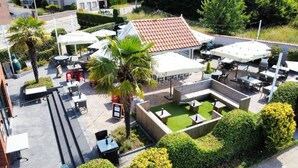 An outdoor patio area with tables and chairs, surrounded by greenery and a building with a red-tiled roof. - Modern Apartment in a Prime Location! (Tongeren)