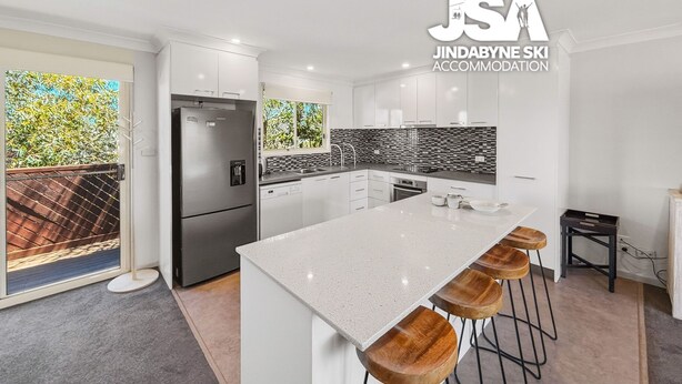Una cocina moderna con muebles blancos, un refrigerador de acero inoxidable, una isla grande con taburetes y un salpicadero blanco y negro.