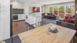Una cocina moderna con armarios blancos, una isla grande y una zona de comedor con mesa de madera.