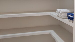 A corner of a room with white walls and a sloped ceiling. There are three white shelves, one of which has folded towels and a blue cloth.