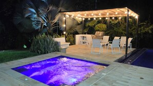 A pool with a water feature and a covered patio area with chairs and a grill.