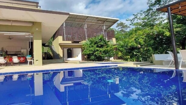 A swimming pool with a covered patio area, a kitchen, and a staircase leading to an upper level.