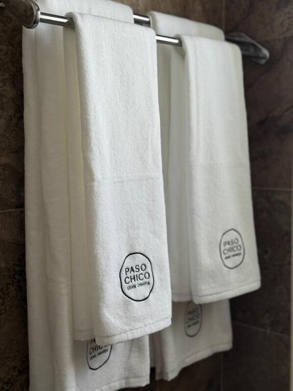Three white towels hanging on a metal towel rack in a bathroom with a tiled wall. - PASO CHICO GRAN CANARIA (San Bartolomé de Tirajana)
