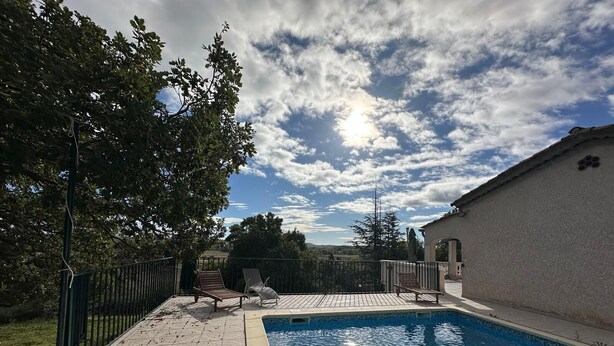 Une piscine avec deux chaises longues et une pergola, le tout entouré d’une clôture et d’arbres.