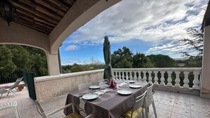 Un espace de restauration en plein air avec une table dressée pour quatre personnes, entourée de chaises blanches dotées de coussins jaunes.