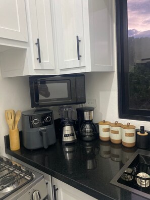 Cuina amb armaris blancs, taule negra, fogó, microones, torradora, batedora, cafetera i pots d'espècies etiquetats com a "tea", "coffee" i "sugar".