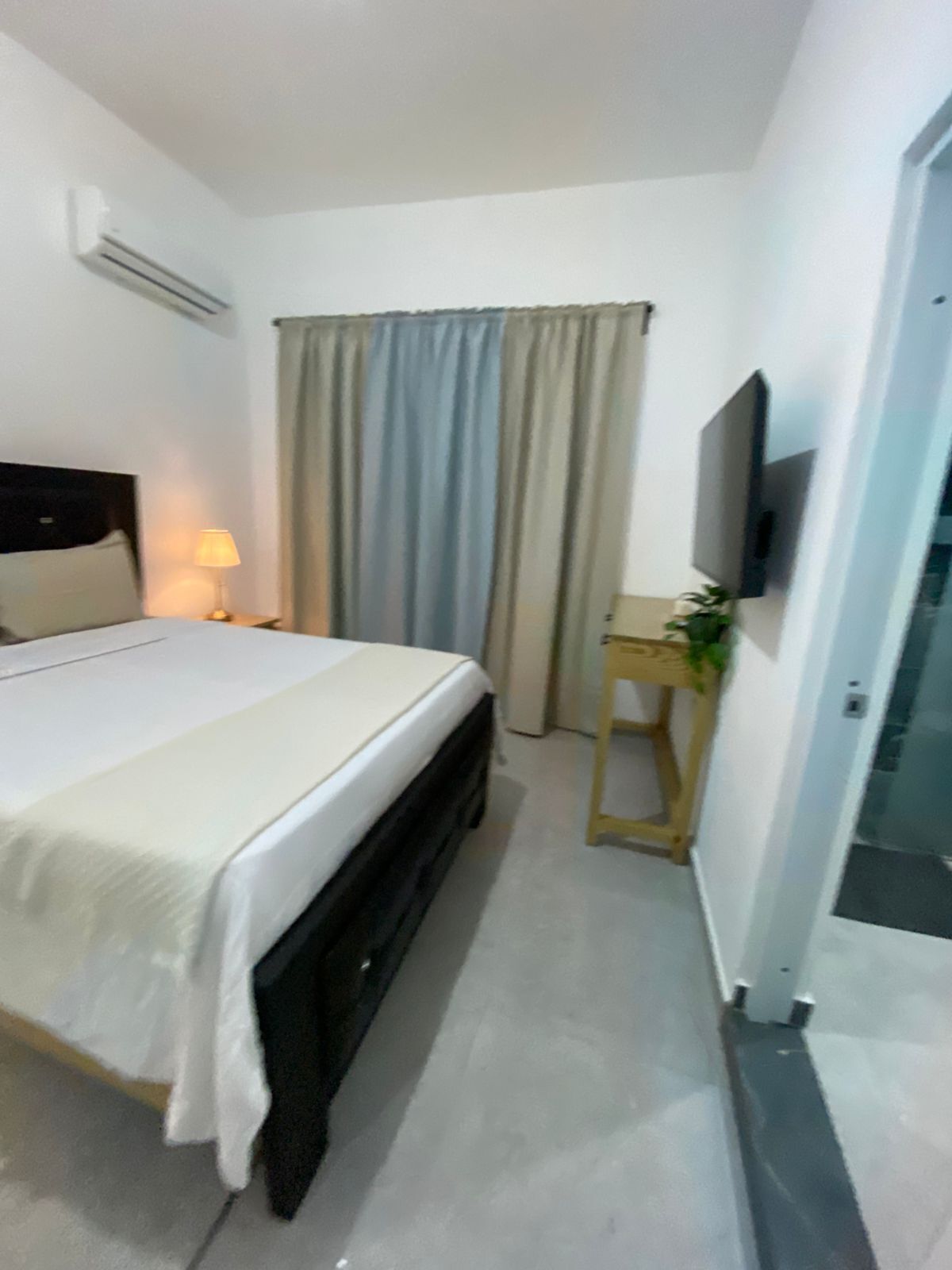Habitación de hotel con cama, escritorio, televisor y ventana con cortinas.