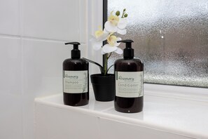 Zwei Flaschen Rosmarin-Shampoo und -Spülung auf einem weißen Regal.