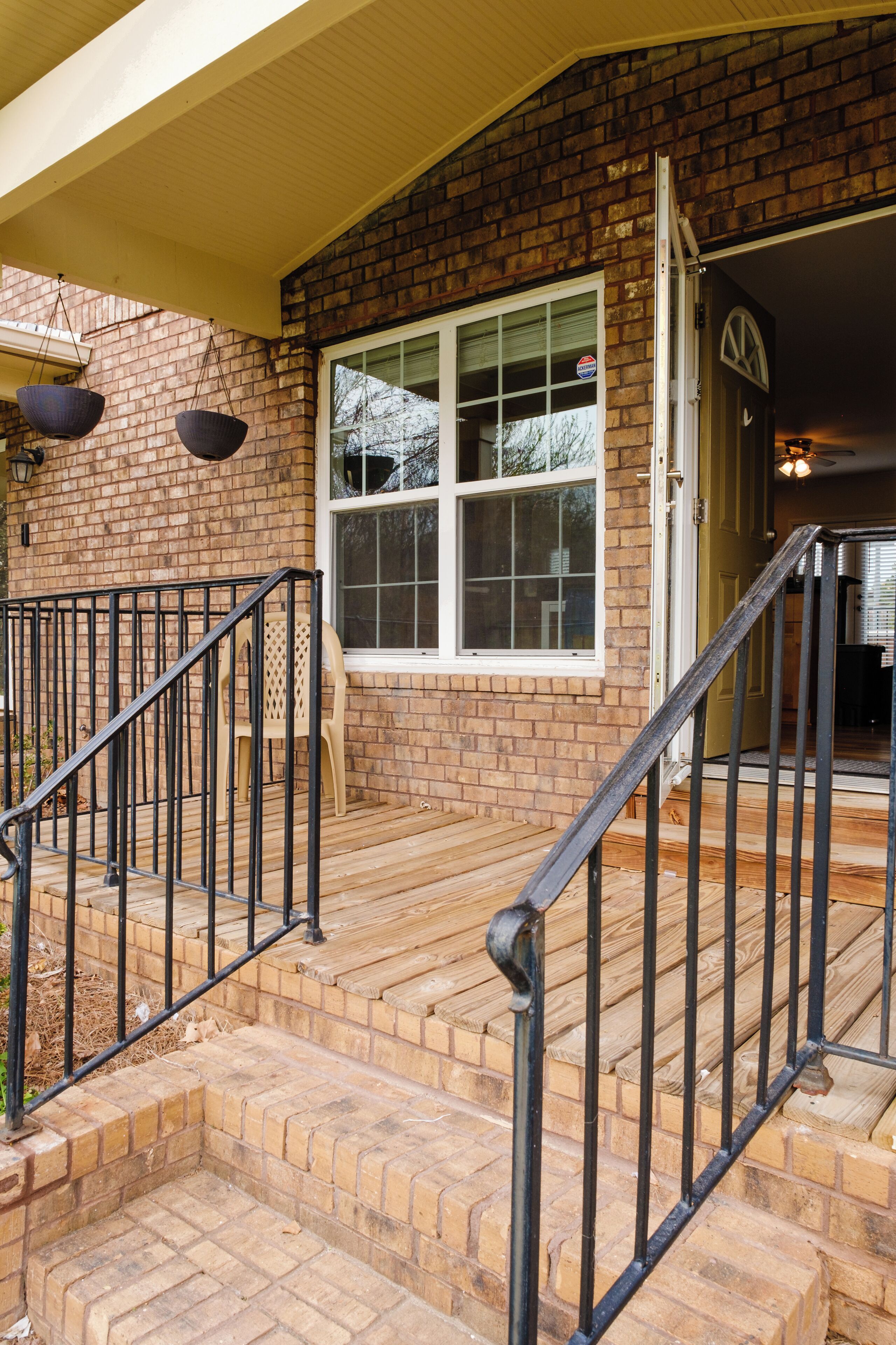 A brick house with a front porch, a set of wooden steps, and a black metal railing.