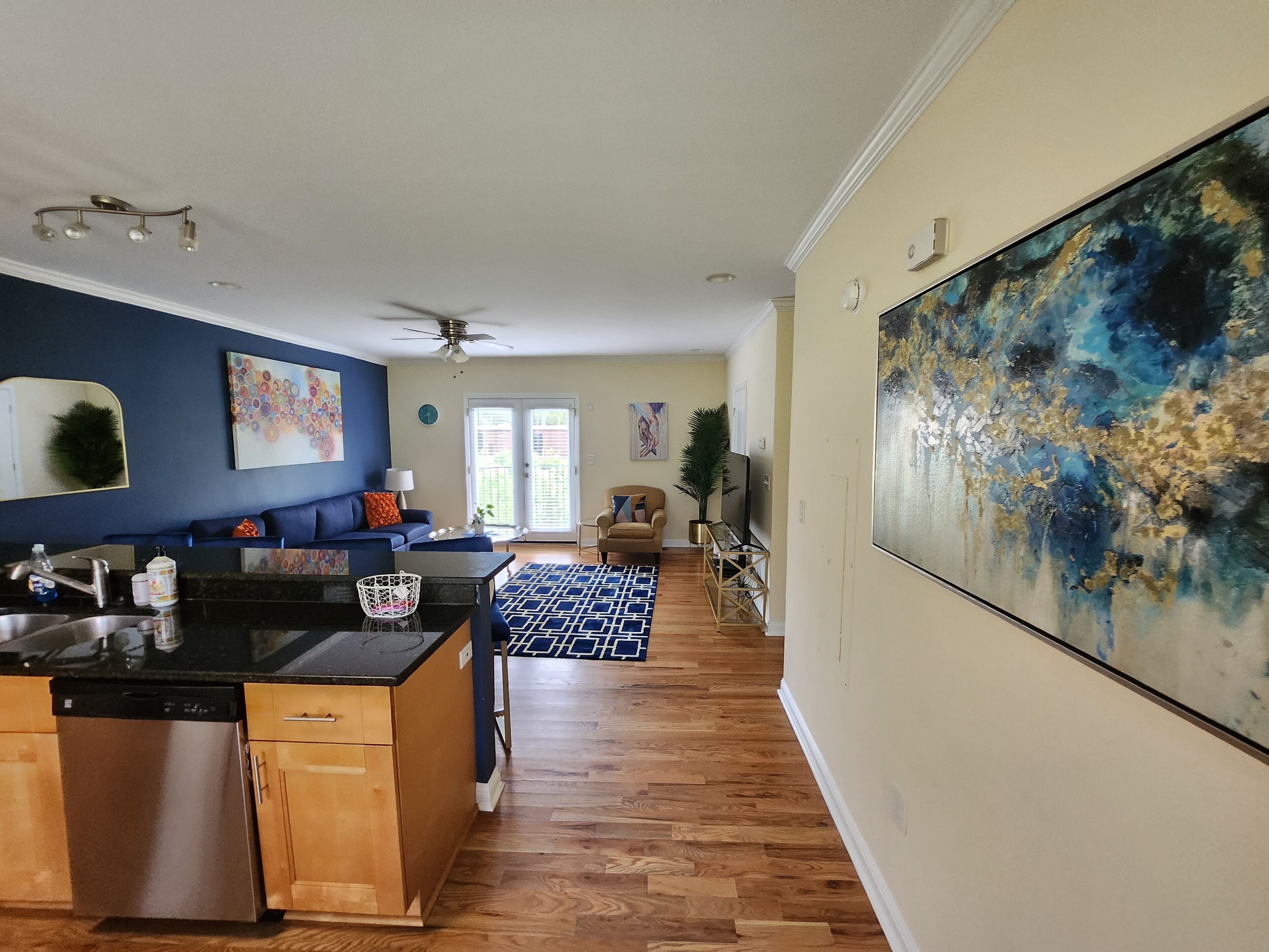 A modern kitchen with a dishwasher, a dining area with a patterned rug, and a large abstract painting on the wall.