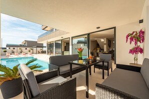 Et moderne udendørs loungeområde med pool, møbler og udsigt til den tilstødende bygning.