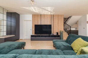 Ein modernes Wohnzimmer mit einem großen Flachbildfernseher, dunklen Sofas und einer Wand als Holzdekor.