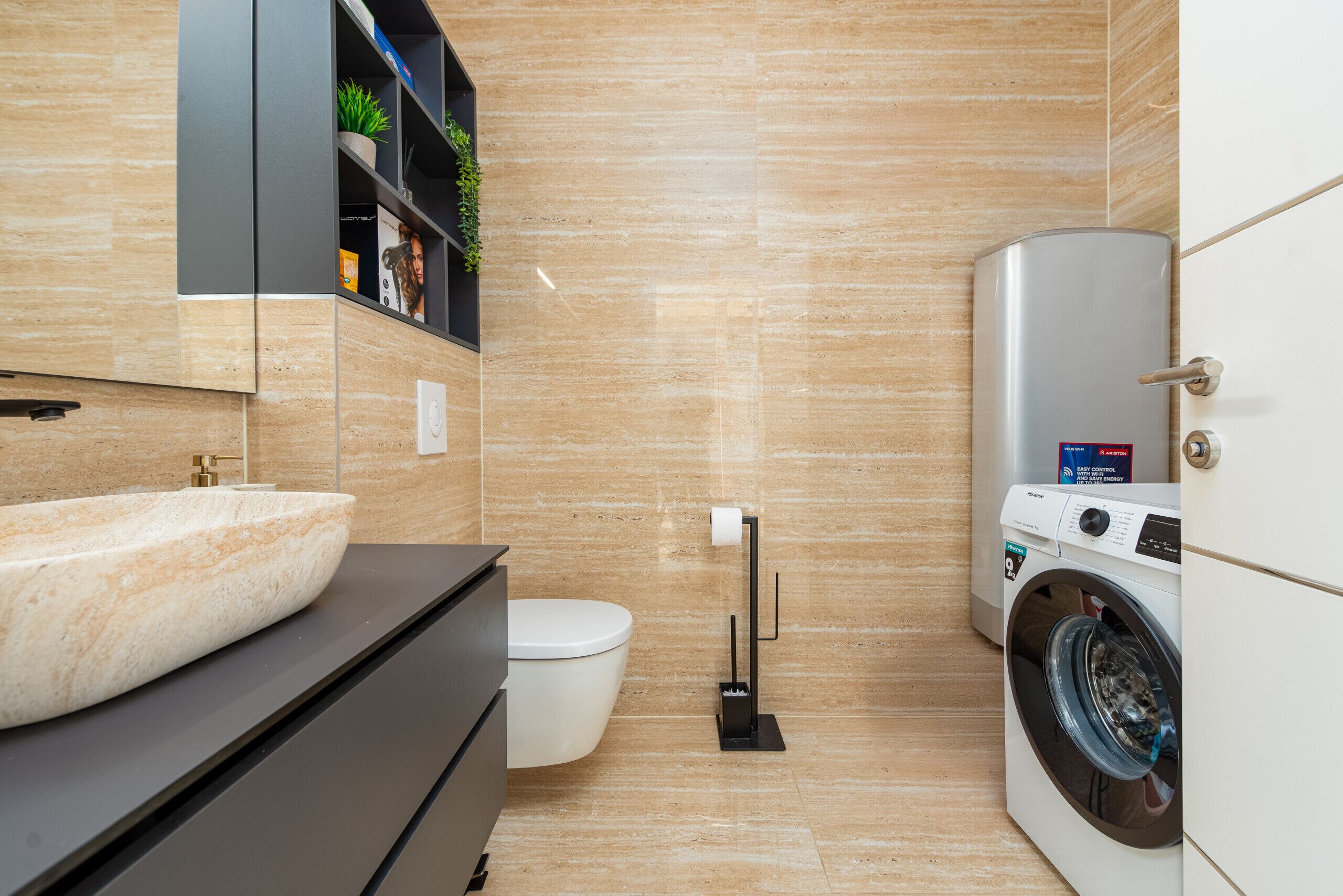 A modern bathroom with a stone sink, toilet, and a front-loading washing machine.