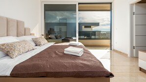 Une chambre moderne avec un grand lit, une vue sur la ville grâce à une porte-fenêtre coulissante et un design minimaliste.