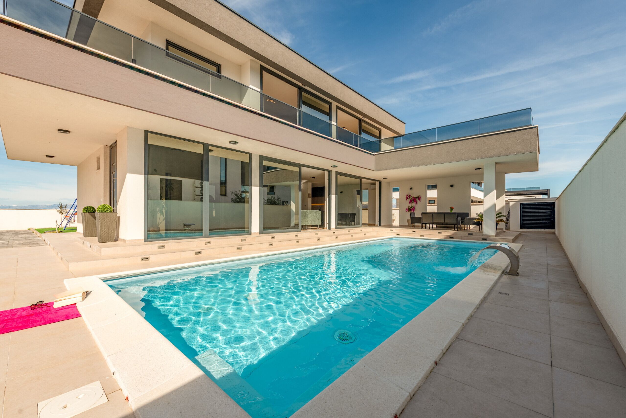 Uma casa moderna de dois andares com piscina, amplas janelas de vidro e uma varanda.