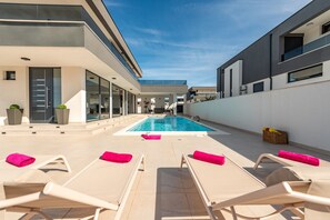 Un área de piscina moderna al aire libre con sillones de descanso y vista despejada a la piscina.
