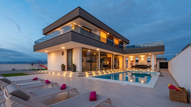Une maison moderne à deux étages, dotée d’une piscine, d’un espace salon extérieur et offrant une vue sur les montagnes.