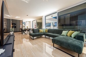 Ein modernes Wohnzimmer mit Ecksofa, Essbereich und durch Glastüren sichtbarer Küche.