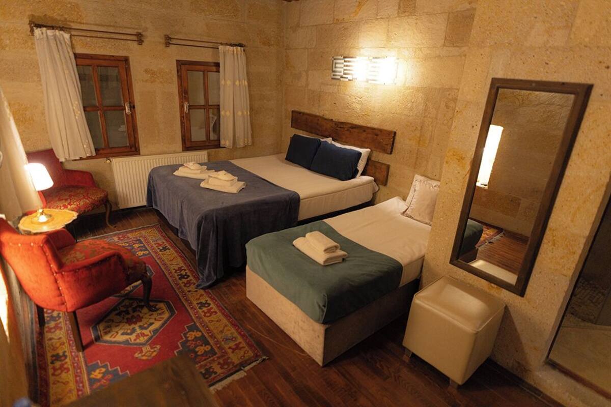 A hotel room with two beds, a red armchair, a small table, a radiator, and a mirror.