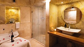 A bathroom with a glass shower, a sink with a mirror, and a bottle of alcohol on the counter. - roca cappadocia suites (Ürgüp)