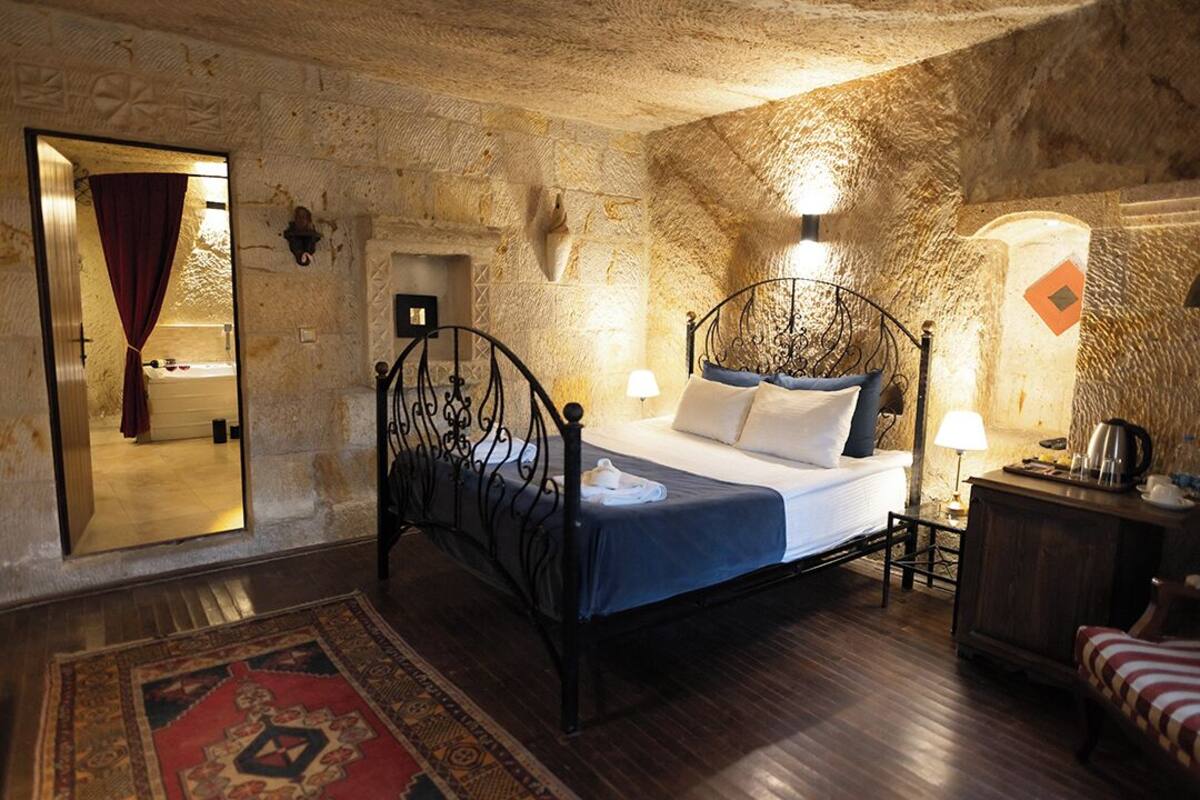 A stone-walled bedroom with a bed, a nightstand, a lamp, and a wooden cabinet.