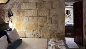 A rustic stone-walled bedroom with a bed, pillows, and a nightstand. - roca cappadocia suites (Ürgüp)