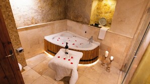 A bathroom with a freestanding bathtub, a small table with rose petals and a bottle, and candles on the floor. - roca cappadocia suites (Ürgüp)