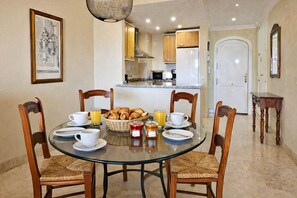 A dining area with a round glass table, four wooden chairs, and a breakfast setting including croissants, juice, and coffee. - Los Patios de Santa Maria Golf, Elviria (Marbella)