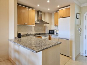 A modern kitchen with granite countertops, stainless steel appliances, wooden cabinets, and a built-in microwave. - Los Patios de Santa Maria Golf, Elviria (Marbella)