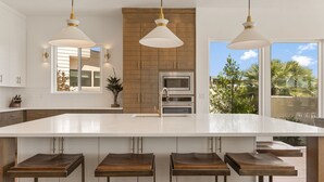 Una cocina moderna con una isla grande, luces colgantes y vistas al exterior.